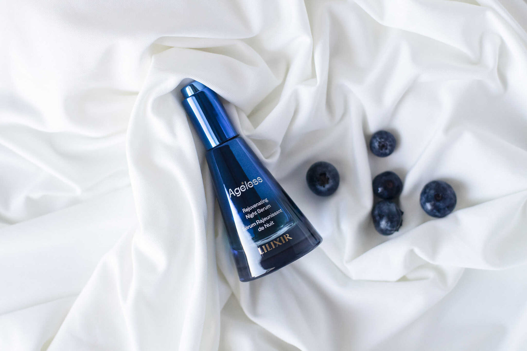 LILIXIR Ageless Rejuvenating Night Serum, a blue serum bottle with blueberries on a white fabric background