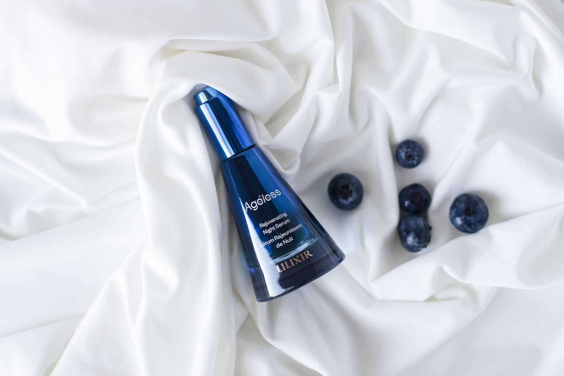 LILIXIR Ageless Rejuvenating Night Serum, a blue serum bottle with blueberries on a white fabric background