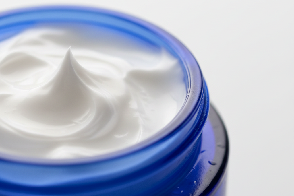 Close-up of a jar of white cream with a blue lid on a light gray background