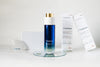 LILIXIR Flawless skincare set featuring a blue gradient bottle with a gold cap, two white product boxes, and a white crystal gua Sha arranged on a white surface with a glass coaster.