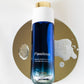 A bottle of Flawless Morning & Evening Cleanser by LILIXIR, featuring a blue gradient liquid, a white cap, and a gold cap, presented on a gold circular prop against a white background.