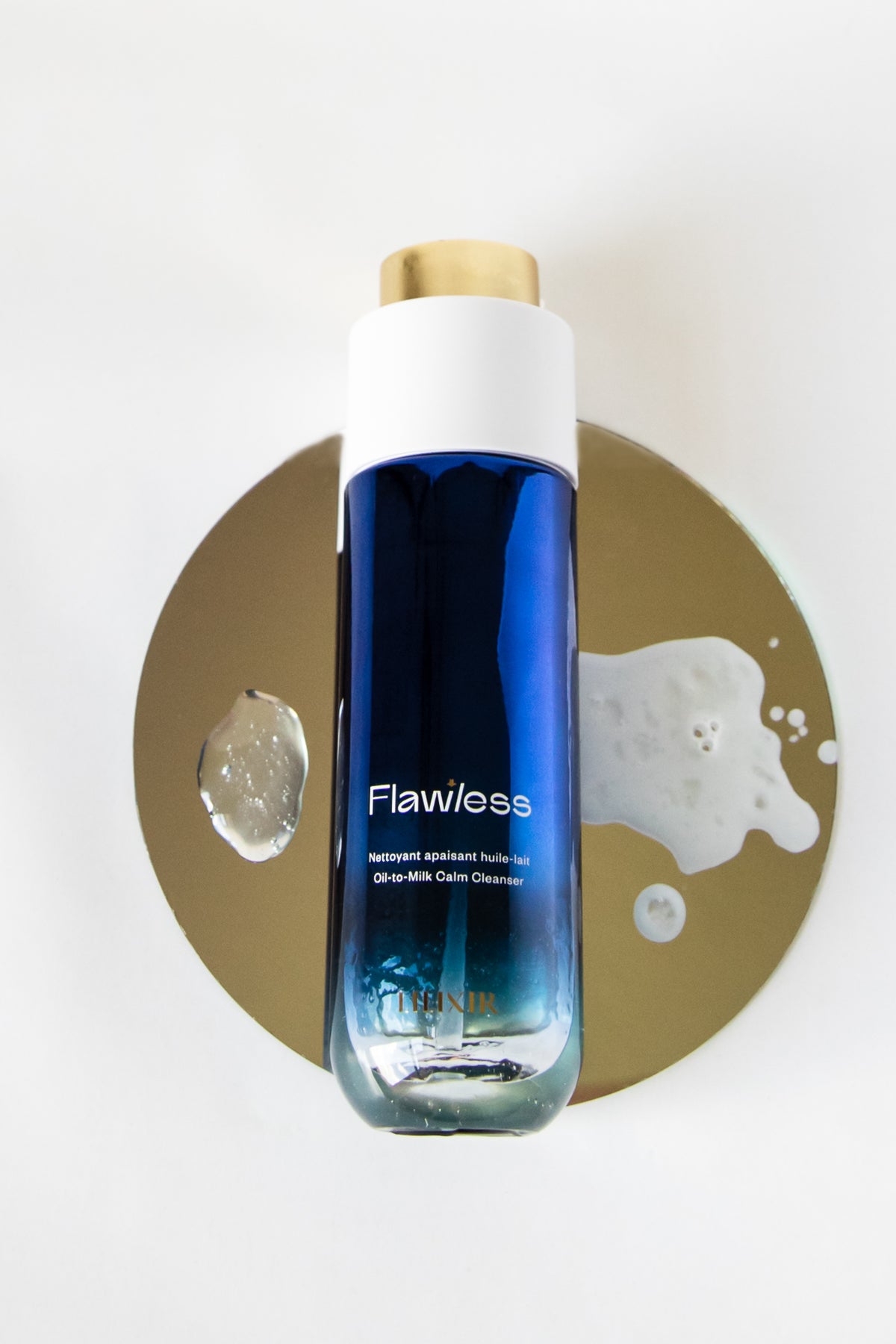 A bottle of Flawless Morning & Evening Cleanser by LILIXIR, featuring a blue gradient liquid, a white cap, and a gold cap, presented on a gold circular prop against a white background.