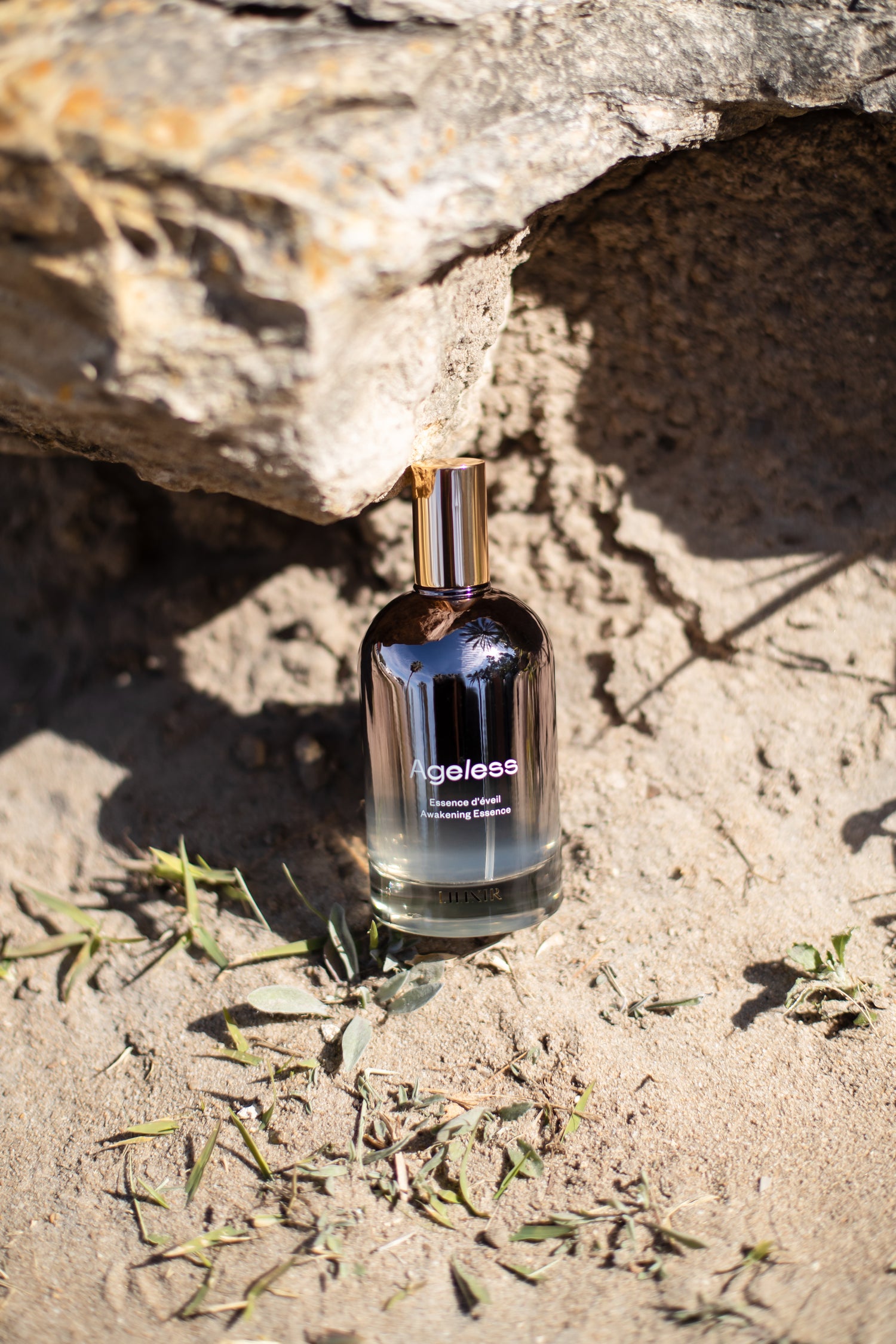 Bottle of LILIXIR Ageless Awakening Essence on a rocky surface with natural light