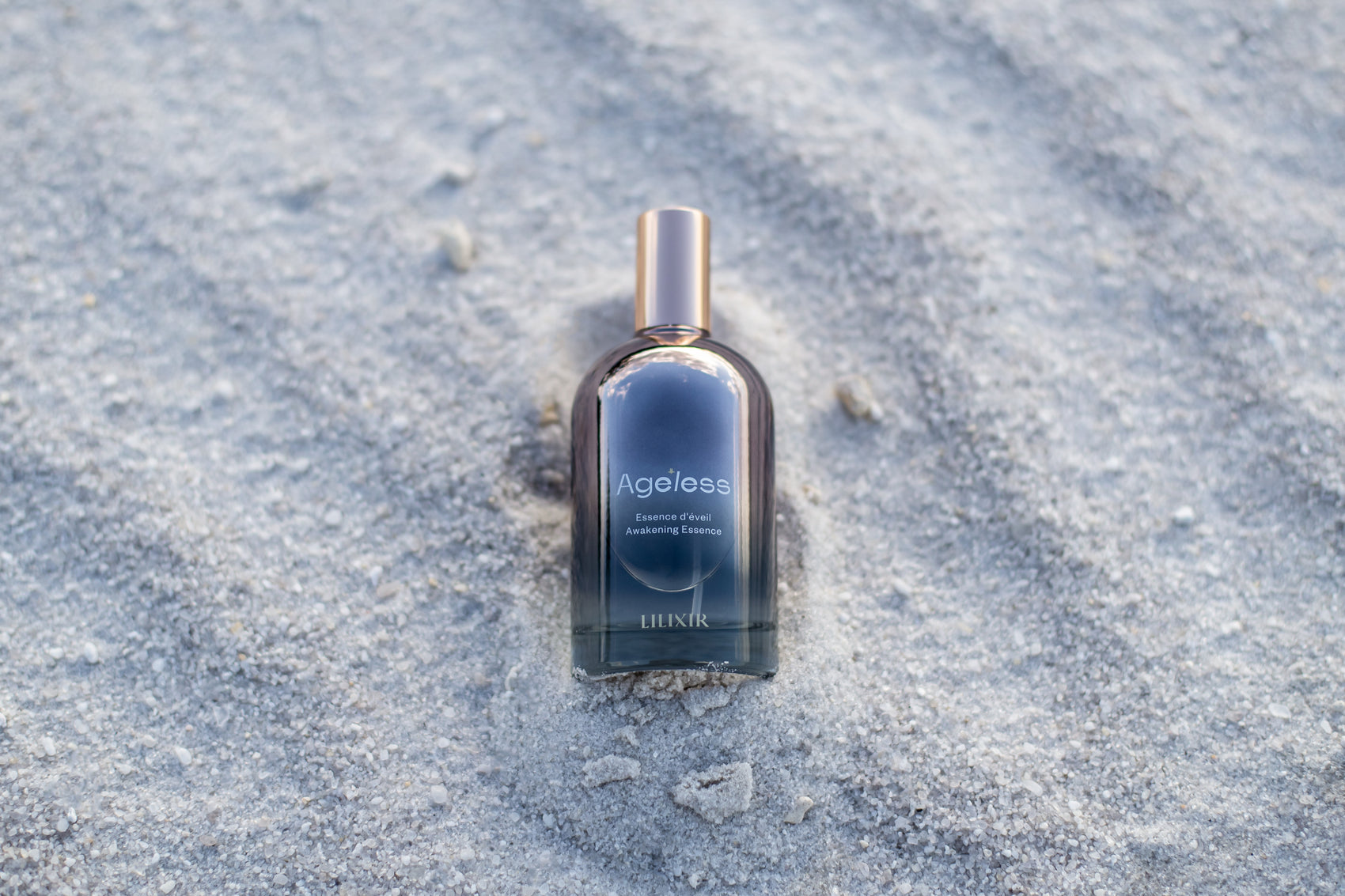 Bottle of 'LILIXIR Ageless Awakening Essence'  on sandy ground