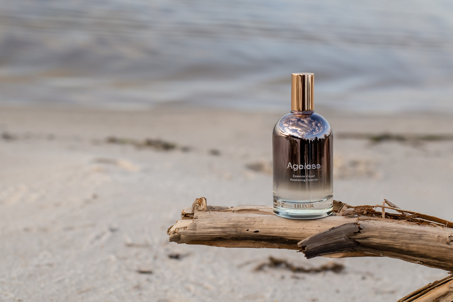 A bottle of lilixir ageless essence on a piece of driftwood by the beach