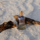 Bottle of 'LILIXIR Ageless Awakening Essence'  on a sandy surface with driftwood