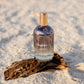 Bottle of 'LILIXIR Ageless Awakening Essence'  on a piece of driftwood in sandy beach setting