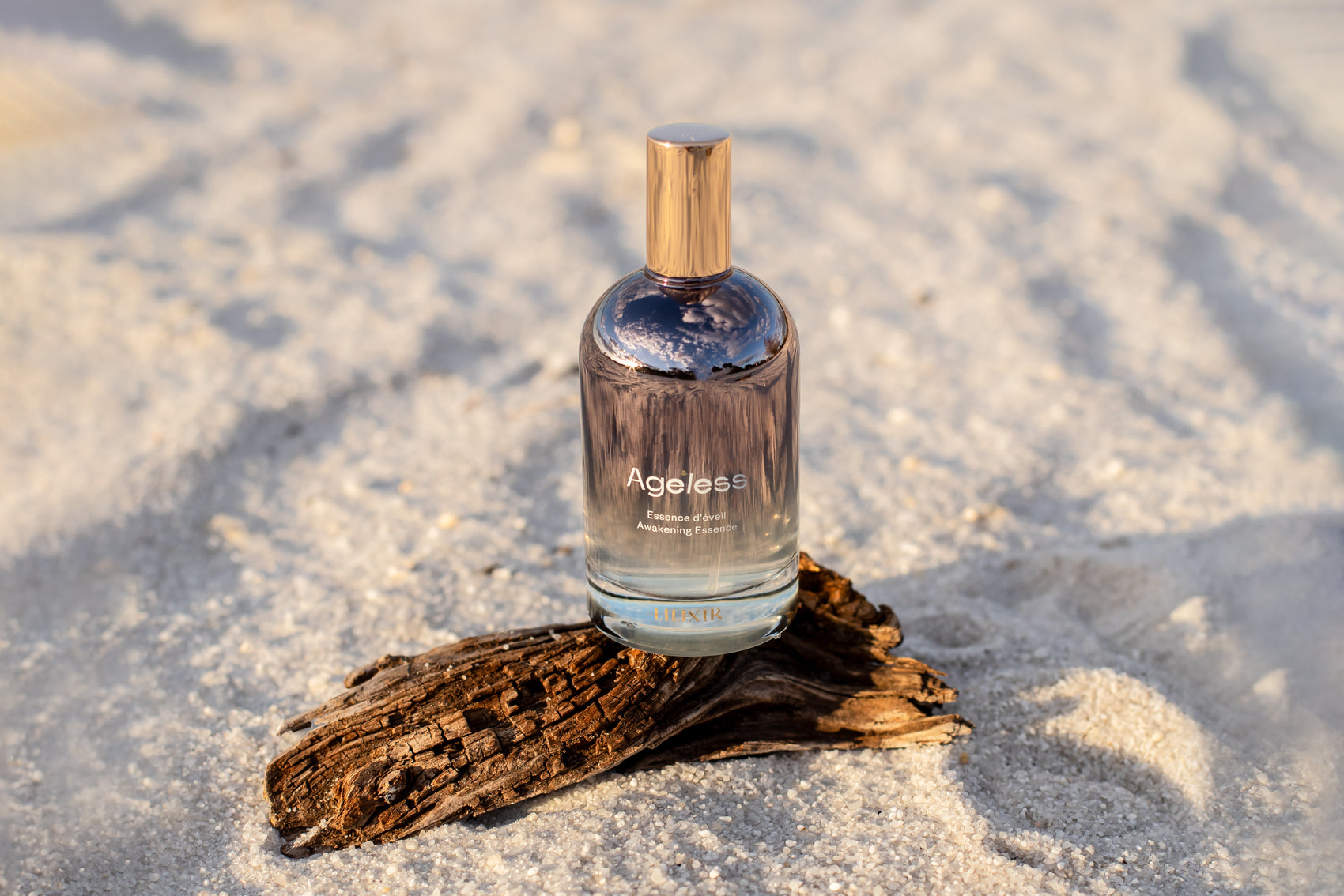 Bottle of 'LILIXIR Ageless Awakening Essence'  on a piece of driftwood in sandy beach setting