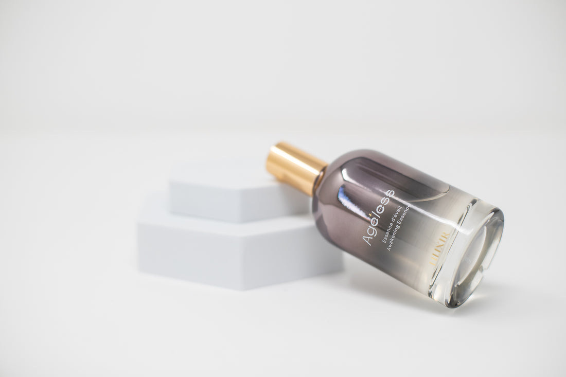 Clear glass bottle of climate adaptive essence with gold cap on a white background