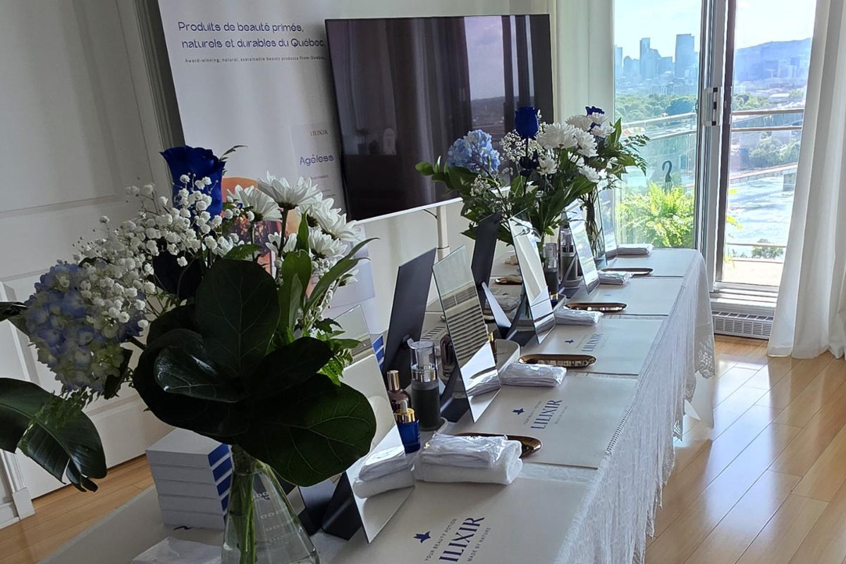 A long white table set up in a bright room with wood floors, featuring floral arrangements, brochures, a tablet, and a branded vertical banner that reads L'EAU.