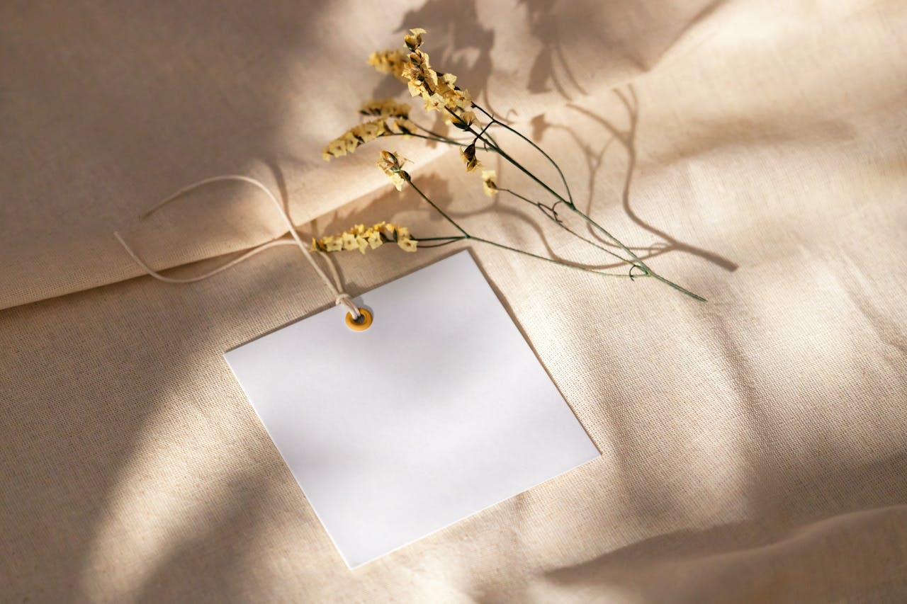 White square card with dried flowers on a beige fabric background, lilixir